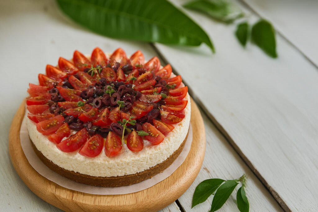 Αλμυρό cheesecake με ντοματίνια και φύλλα βασιλικού πάνω σε ξύλινη βάση.