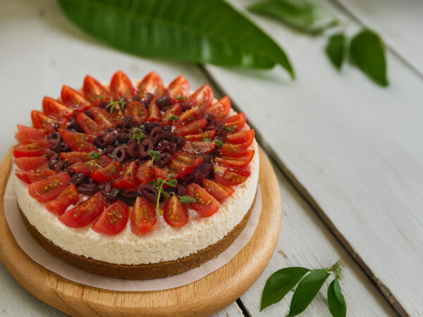 Αλμυρό cheesecake με ντοματίνια και φύλλα βασιλικού πάνω σε ξύλινη βάση.