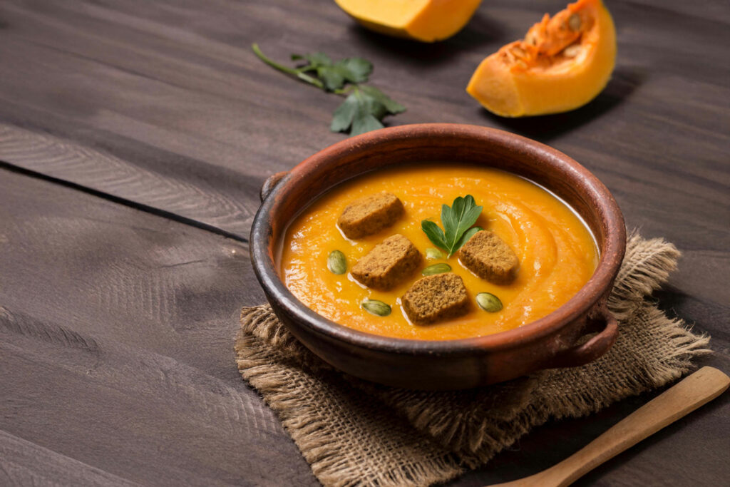 Κολοκυθόσουπα σε μπολ με παξιμάδια ολικής και γιαούρτι, σερβιρισμένη με κολοκύθα.