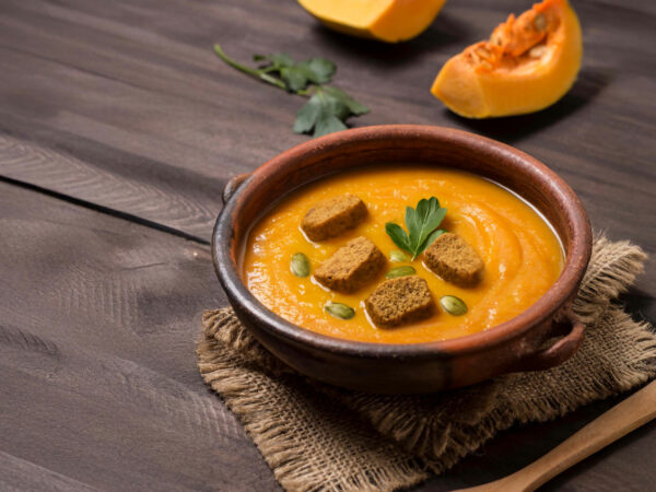 Κολοκυθόσουπα σε μπολ με παξιμάδια ολικής και γιαούρτι, σερβιρισμένη με κολοκύθα.